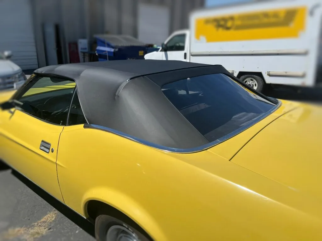 A classic, yellow 1973 Ford Mustang with a new, black soft top installed. 